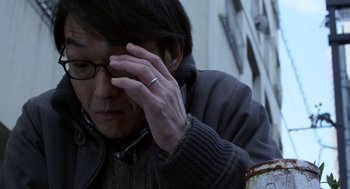 Movie still from “Cold Fish” (2010), directed by Sion Sono – A man with glasses is holding his hand up to his face; Close Up shot, Low angle