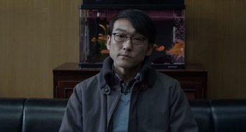 Movie still from “Cold Fish” (2010), directed by Sion Sono – A man sitting in front of a fish tank; Close Up shot, Over the shoulder angle
