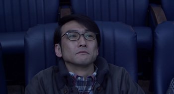 Movie still from “Cold Fish” (2010), directed by Sion Sono – A man sitting in a chair with his eyes wide open; Close Up shot, High angle