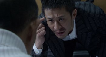 Movie still from “Cold Fish” (2010), directed by Sion Sono – A man in a suit is talking to another man in a suit; Close Up shot, High angle