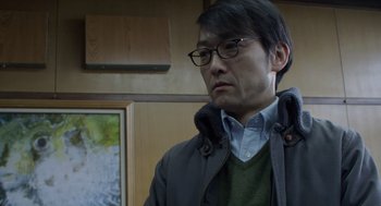 Movie still from “Cold Fish” (2010), directed by Sion Sono – A man with glasses is looking down at the ceiling; Close Up shot, Over the shoulder angle