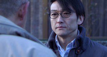 Movie still from “Cold Fish” (2010), directed by Sion Sono – A person wearing glasses and a jacket; Close Up shot, Over the shoulder angle