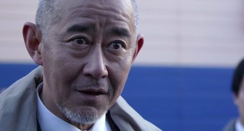 Movie still from “Cold Fish” (2010), directed by Sion Sono – An older man wearing a white shirt and a tie; Close Up shot, Over the shoulder angle