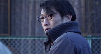 Movie still from “Cold Fish” (2010), directed by Sion Sono – A person wearing glasses and a jacket; Close Up shot, Low angle