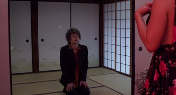 Movie still from “Cold Fish” (2010), directed by Sion Sono – A man sitting on the ground in a room; Medium shot, Low angle