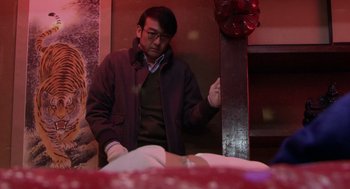 Movie still from “Cold Fish” (2010), directed by Sion Sono – A man standing next to a bed in a room; Medium shot, Low angle