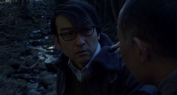 Movie still from “Cold Fish” (2010), directed by Sion Sono – A man with glasses is looking at the camera while another man looks at him; Close Up shot, Over the shoulder angle