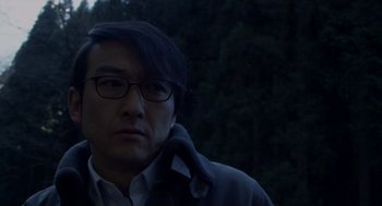 Movie still from “Cold Fish” (2010), directed by Sion Sono – A man wearing glasses and a jacket in the dark; Close Up shot, Low angle