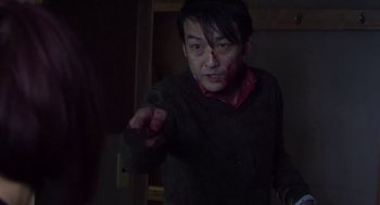 Movie still from “Cold Fish” (2010), directed by Sion Sono – A man in a dark room with blood on his face; Medium shot, Over the shoulder angle