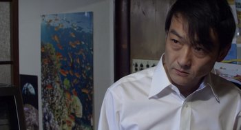 Movie still from “Cold Fish” (2010), directed by Sion Sono – A person wearing a white shirt; Close Up shot, Over the shoulder angle