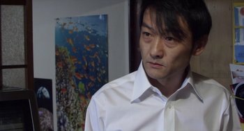 Movie still from “Cold Fish” (2010), directed by Sion Sono – A man wearing a white shirt standing in front of an aquarium; Close Up shot, Over the shoulder angle