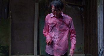 Movie still from “Cold Fish” (2010), directed by Sion Sono – A man in a pink shirt is holding a knife in his hand; Medium shot, Low angle