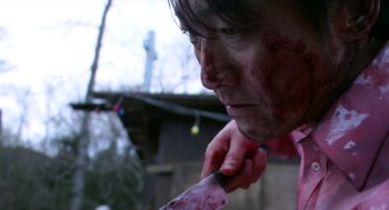 Movie still from “Cold Fish” (2010), directed by Sion Sono – A man with blood on his face holding a knife; Close Up shot, Low angle