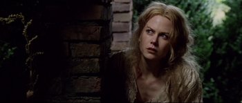Movie still from “Cold Mountain” (2003), directed by Anthony Minghella – A woman with blonde hair is looking at the camera while standing next to a brick wall; Close Up shot, Low angle