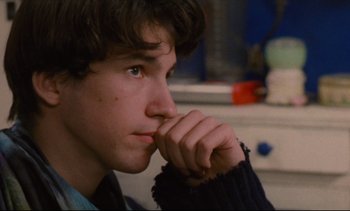 Movie still from “Cold Water” (1994), directed by Olivier Assayas – A young man is looking into the distance with his hand under his chin; Close Up shot, Over the shoulder angle