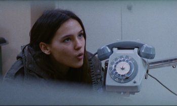 Movie still from “Cold Water” (1994), directed by Olivier Assayas – A woman holding up a phone in front of her face; Close Up shot, Low angle