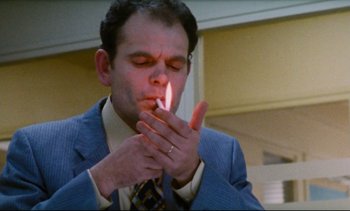 Movie still from “Cold Water” (1994), directed by Olivier Assayas – A man in a suit and tie lighting a cigarette; Close Up shot, Low angle