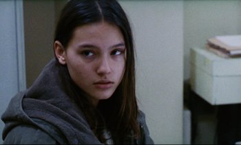 Movie still from “Cold Water” (1994), directed by Olivier Assayas – A young woman with long dark brown hair wearing a gray jacket; Close Up shot, Over the shoulder angle