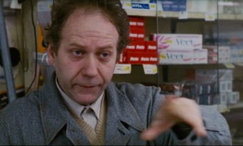 Movie still from “Cold Water” (1994), directed by Olivier Assayas – A man in a gray jacket is pointing to a wall; Close Up shot, Over the shoulder angle