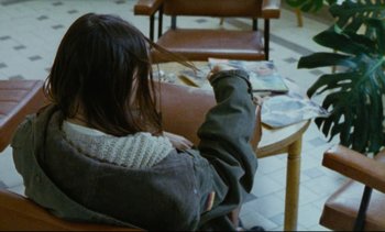 Movie still from “Cold Water” (1994), directed by Olivier Assayas – A person sitting on a chair in a room; Medium shot, Over the shoulder angle