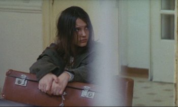 Movie still from “Cold Water” (1994), directed by Olivier Assayas – A woman sitting on top of a chair with her arms crossed; Medium shot, High angle