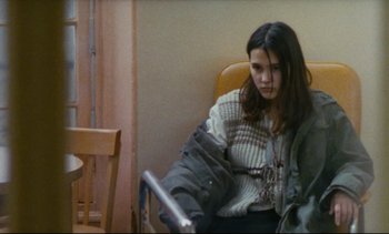 Movie still from “Cold Water” (1994), directed by Olivier Assayas – A woman sitting in a chair looking at a book; Medium shot, High angle