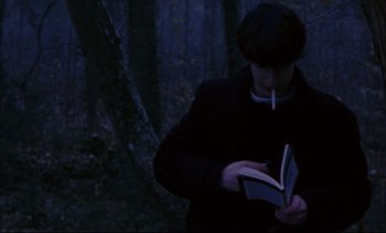 Movie still from “Cold Water” (1994), directed by Olivier Assayas – A man smoking a cigarette while reading a book; Medium shot, Over the shoulder angle