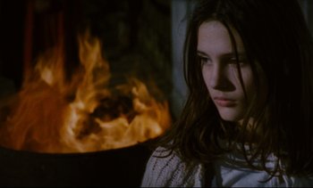 Movie still from “Cold Water” (1994), directed by Olivier Assayas – A woman is standing in front of a fire; Close Up shot, Over the shoulder angle
