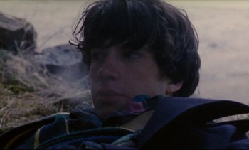 Movie still from “Cold Water” (1994), directed by Olivier Assayas – A young man is smoking a cigarette in a field; Close Up shot, High angle