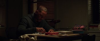 Movie still from “Collateral Beauty” (2016), directed by David Frankel – A man sitting at a table cutting paper with scissors; Medium shot, High angle