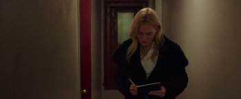 Movie still from “Collateral Beauty” (2016), directed by David Frankel – A woman writing in a notebook while standing next to a door; Medium shot, Over the shoulder angle