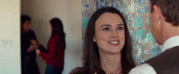 Movie still from “Collateral Beauty” (2016), directed by David Frankel – A young woman smiles brightly while standing in front of a wall; Close Up shot, Over the shoulder angle