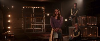 Movie still from “Collateral Beauty” (2016), directed by David Frankel – A woman in a purple sweater holding a book; Medium shot, Over the shoulder angle