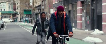 Movie still from “Collateral Beauty” (2016), directed by David Frankel – A man riding a bike down a street next to another man; Medium shot, Low angle
