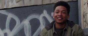 Movie still from “Collateral Beauty” (2016), directed by David Frankel – A young man smiles in front of a graffiti wall; Close Up shot, Over the shoulder angle