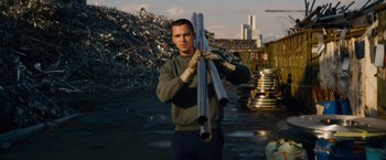 Movie still from “Collide” (2016), directed by Eran Creevy – A man holding a bunch of metal pipes in his hands; Medium shot, Low angle
