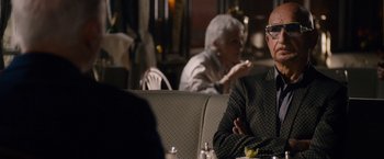 Movie still from “Collide” (2016), directed by Eran Creevy – A man sitting at a table in front of an older woman; Medium shot, Over the shoulder angle