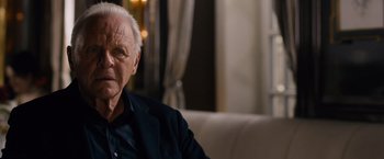 Movie still from “Collide” (2016), directed by Eran Creevy – An older man sitting on a couch in front of a window; Close Up shot, Over the shoulder angle