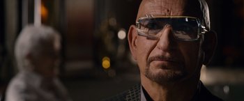 Movie still from “Collide” (2016), directed by Eran Creevy – An older man wearing glasses and a suit; Close Up shot, Over the shoulder angle
