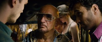 Movie still from “Collide” (2016), directed by Eran Creevy – An older man with glasses and a woman behind him; Close Up shot, Over the shoulder angle