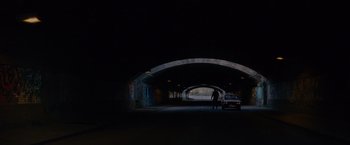 Movie still from “Collide” (2016), directed by Eran Creevy – A person standing in a dark tunnel with a car; Extreme Wide shot, High angle