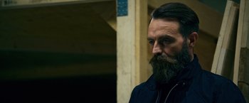 Movie still from “Collide” (2016), directed by Eran Creevy – A man with a long beard and a goatee looking to his left; Close Up shot, Low angle