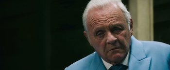 Movie still from “Collide” (2016), directed by Eran Creevy – An older man wearing a blue suit and a blue tie; Close Up shot, Low angle