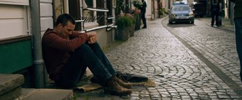 Movie still from “Collide” (2016), directed by Eran Creevy – A man sitting on the ground next to a woman on the sidewalk; Wide shot, High angle