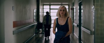Movie still from “Collide” (2016), directed by Eran Creevy – A woman in a blue dress is standing in a hallway; Medium shot, Over the shoulder angle