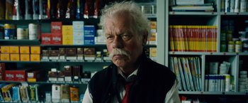 Movie still from “Collide” (2016), directed by Eran Creevy – An old man with a white beard wearing a red tie; Close Up shot, Low angle