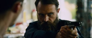 Movie still from “Collide” (2016), directed by Eran Creevy – A man with a long beard is looking at the camera; Close Up shot, Low angle