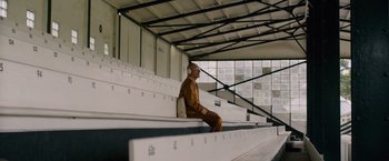 Movie still from “Collide” (2016), directed by Eran Creevy – A man sitting on a bench wearing headphones; Wide shot, High angle