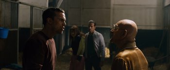 Movie still from “Collide” (2016), directed by Eran Creevy – A group of people standing in a room; Medium shot, Over the shoulder angle