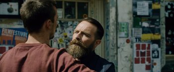 Movie still from “Collide” (2016), directed by Eran Creevy – A man with a long beard is talking to another man; Close Up shot, Over the shoulder angle
